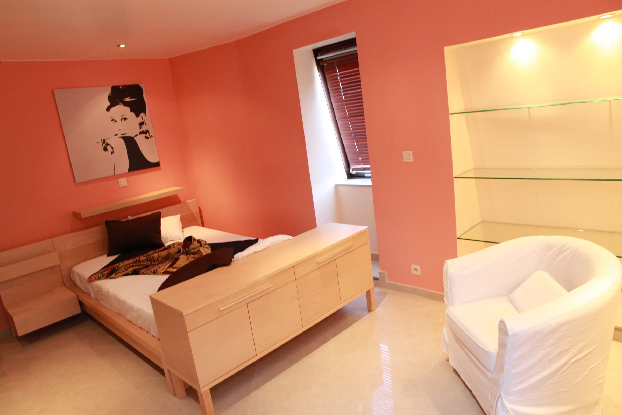 Een slaapkamer met een bed, nachtkastje en een witte stoel.