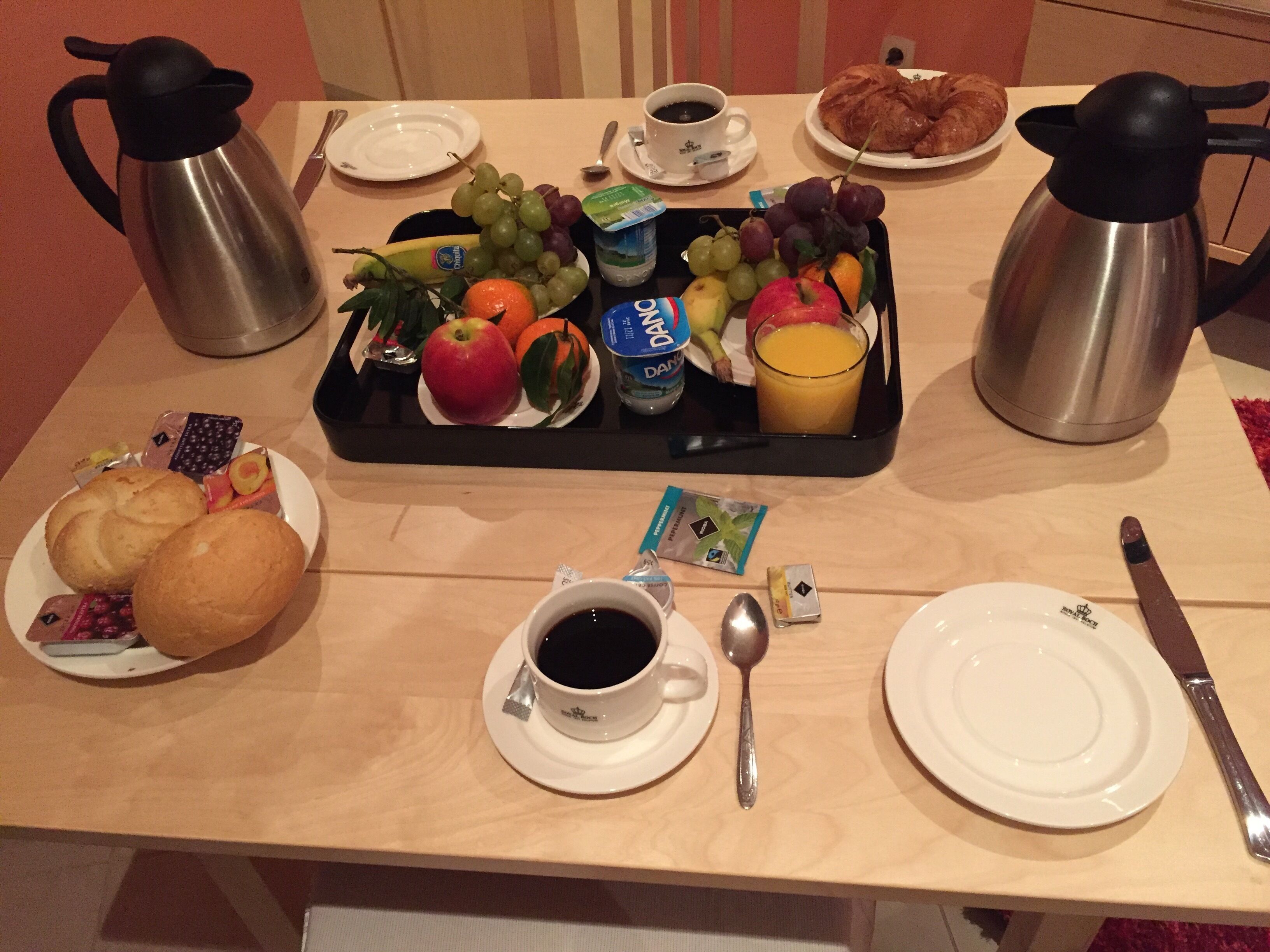 A breakfast tray with fruits, juice, and pastries on a hotel table.