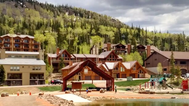 Un albergue con varias cabañas de madera, un parque infantil y un lago.