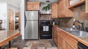 Una cocina con armarios de madera, un refrigerador de acero inoxidable, una estufa negra y una encimera de granito.