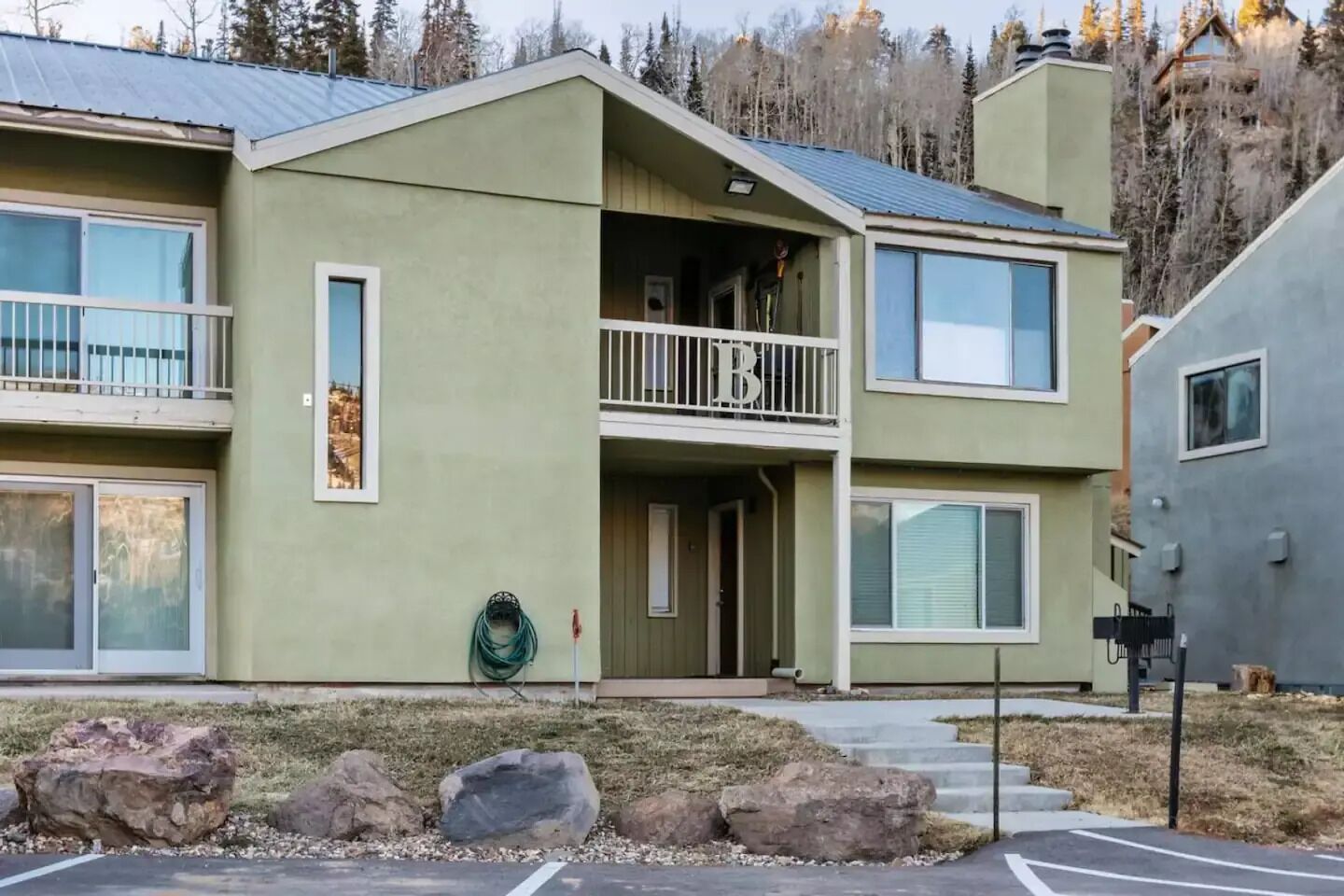 A two-story building with a balcony on the second floor, a visible garage door, and a landscaped front yard with rocks.