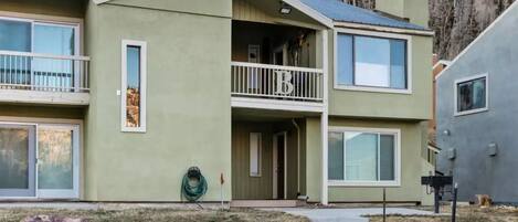 A two-story building with a balcony on the second floor, a visible garage door, and a landscaped front yard with rocks.
