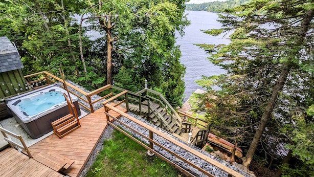 Eine Holzterrasse mit Whirlpool, einer Treppe und Blick auf einen von Bäumen umgebenen See.