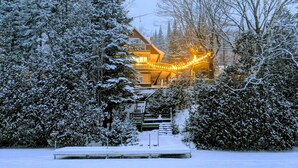 Schneebedeckte Landschaft mit einer Holzhütte, die einen Balkon und eine Treppe zu einer zweiten Ebene besitzt.