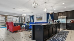 A modern kitchen with dark cabinetry, a central island, stainless steel appliances, and pendant lighting. - Solara Sunshine (Kissimmee)