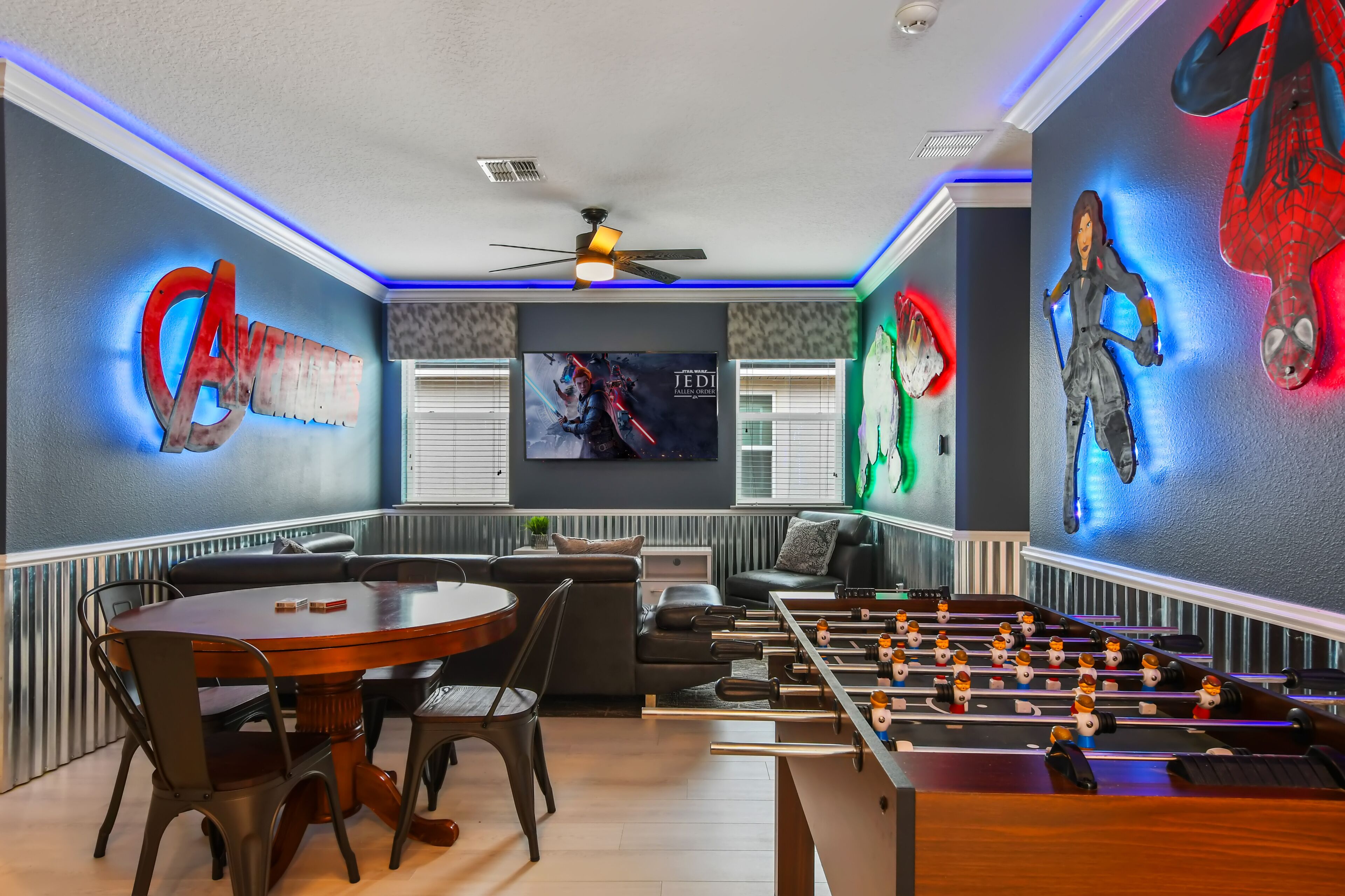 A room with a foosball table, a TV mounted on the wall, and a large Star Wars poster.