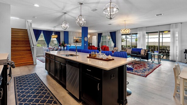 A spacious living area with a large island, blue and red furniture, and a kitchen with modern appliances. - Solara Sunshine (Kissimmee)