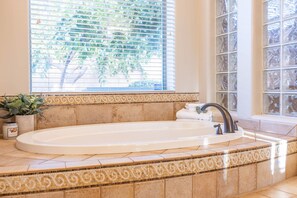 Une salle de bain avec une baignoire sur pieds, une fenêtre avec des stores et une bordure décorative en carreaux.