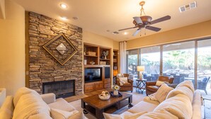 A spacious living room with a stone fireplace, a large flat-screen TV, comfortable seating, and a view of the outdoors. - Gilbert 4BR Villa|Heated Pool+Games|Sleeps 12 (Gilbert)