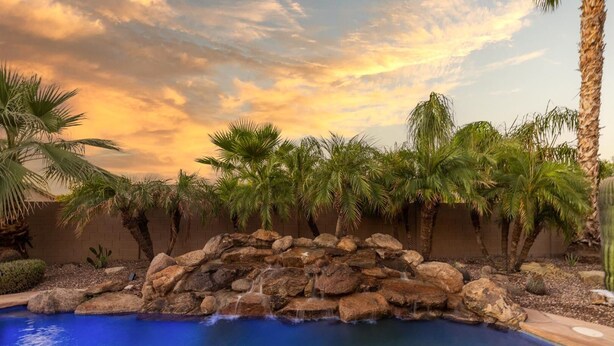 A pool with a waterfall feature surrounded by palm trees and a brick wall. - Gilbert 4BR Villa|Heated Pool+Games|Sleeps 12 (Gilbert)