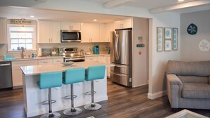Een moderne keuken met witte kasten, roestvrijstalen apparatuur en een centraal eiland met barstoelen.