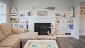 Een woonkamer met een witte open haard, boekenkasten en een nautische inrichting.