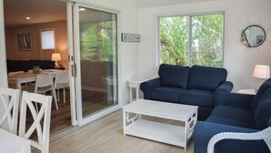 Een woonkamer met een blauwe bank, een witte salontafel en een glazen deur die leidt naar een eetruimte.