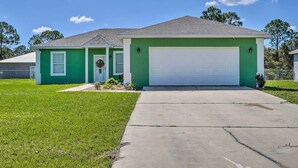 Une maison de plain-pied à l’extérieur vert, avec une porte de garage blanche et une cour avant avec un trottoir menant à l’entrée.