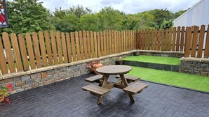 A patio with a wooden table and benches, surrounded by a stone wall and a wooden fence.