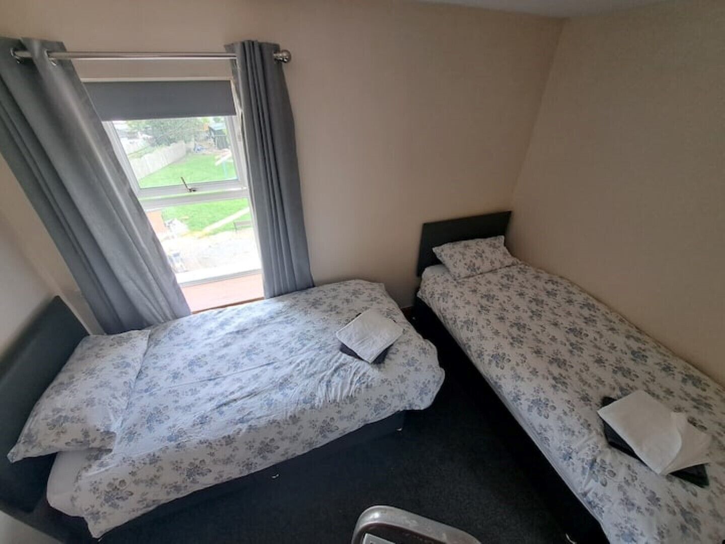 Una habitación de hotel pequeña y con una cama doble, una ventana con cortinas y vistas a un espacio verde exterior.
