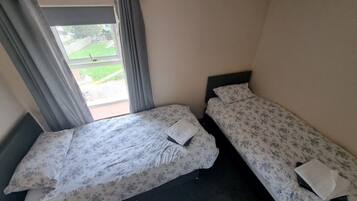 Una habitación de hotel pequeña y con una cama doble, una ventana con cortinas y vistas a un espacio verde exterior.