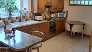 A modern kitchen with wooden cabinets, a central island with bar stools, a built-in oven, and a window providing natural light.