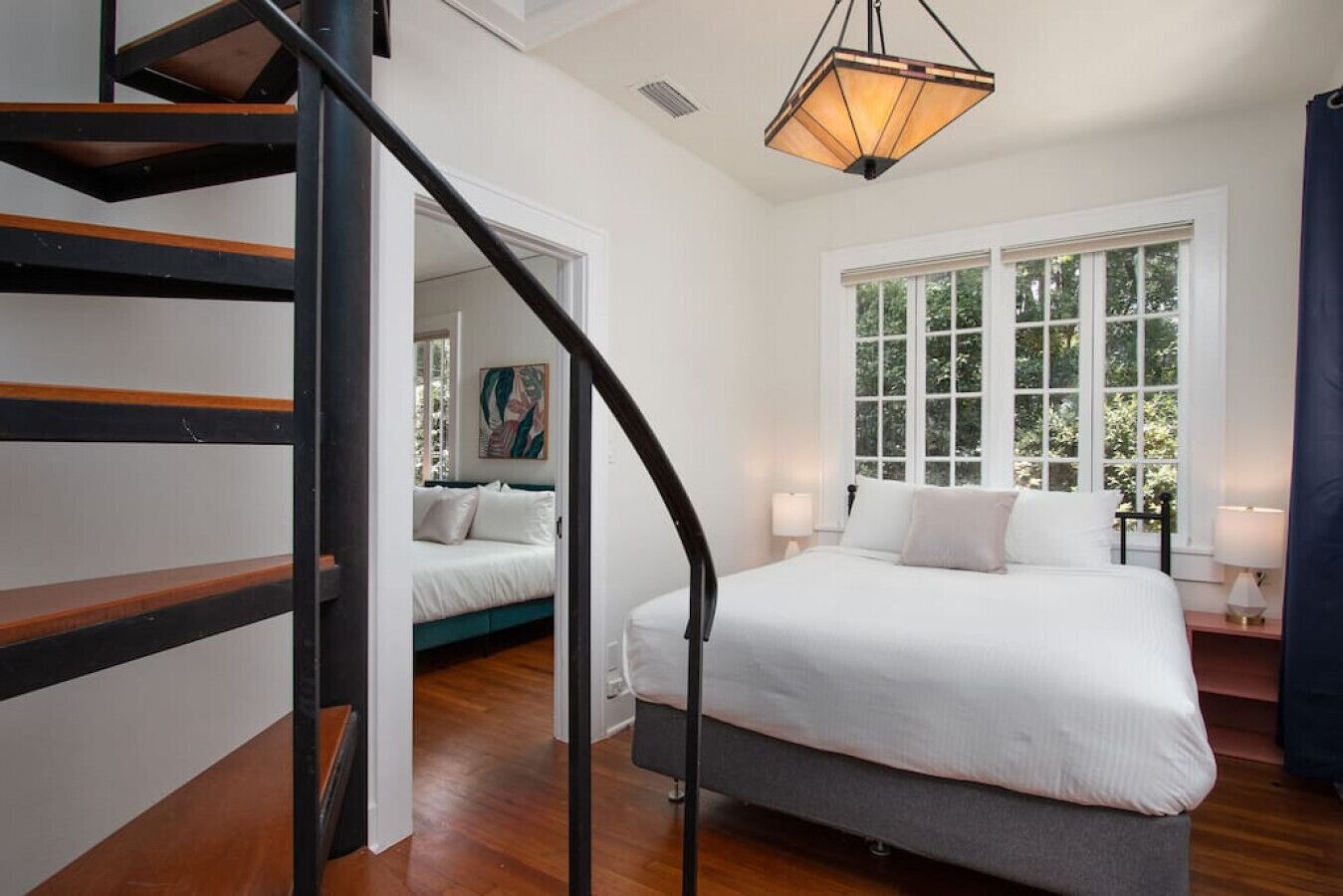 Une chambre avec un grand lit, un escalier et une fenêtre donnant sur des arbres.