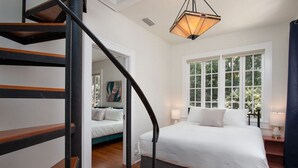 A bedroom with a large bed, a staircase, and a window with a view of trees. - Walk to UF Stadium! Fabulous Chic Historic Home (Gainesville)
