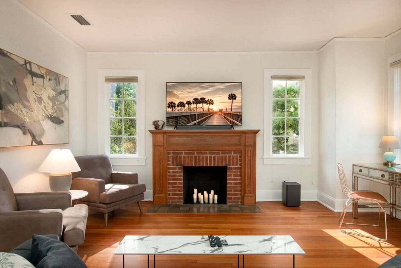 Un salon avec une cheminée, deux fenêtres et un tableau accroché au mur.