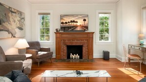 A living room with a fireplace, two windows, and a painting on the wall. - Walk to UF Stadium! Fabulous Chic Historic Home (Gainesville)
