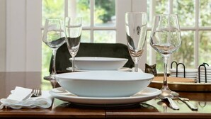 A dining table set with white plates, clear glasses, and cutlery, with a view of greenery through the window. - Walk to UF Stadium! Fabulous Chic Historic Home (Gainesville)