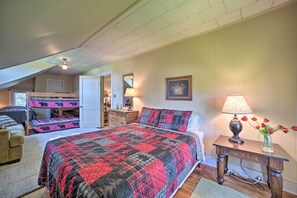 Een slaapkamer met een groot bed, een houten nachtkastje, een lamp en een vaas met bloemen.