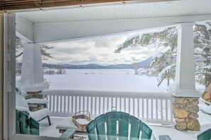 Een overdekte veranda met een stenen pilaar, een witte balustrade en uitzicht op een besneeerd landschap met bergen op de achtergrond.
