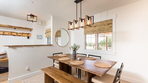 Un coin repas avec une table en bois, des sets de table en fibres tressées et un luminaire suspendu.