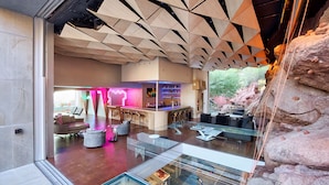 A modern interior with a bar area, seating, and a glass enclosure with a view. - Camelback Vista - 4BR Luxury Estate w/ Infinity Pool & Camelback Views (Phoenix)
