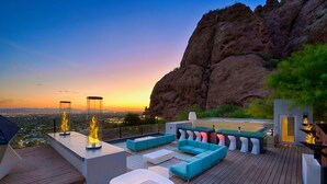 A rooftop terrace with a modern design, featuring a seating area with sofas and chairs, a bar area, and a view of the cityscape at sunset. - Camelback Vista - 4BR Luxury Estate w/ Infinity Pool & Camelback Views (Phoenix)