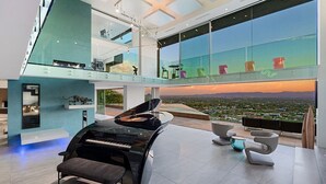 A spacious living area with a grand piano, modern furniture, and a panoramic city view. - Camelback Vista - 4BR Luxury Estate w/ Infinity Pool & Camelback Views (Phoenix)