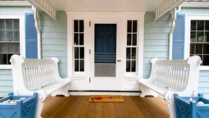 A porch with two white benches, a door with glass panels, and a blue doorbell mat.