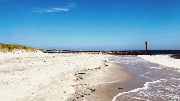 A beach with a lighthouse, sandy shore, and a breakwater.