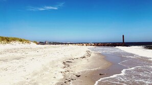 Ein Strand mit Leuchtturm, sandigem Ufer und einer Wellenbrecher-Anlage.