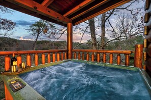 Uma banheira de hidromassagem com deck e guarda-corpo de madeira, cercada por árvores e uma vista da paisagem.
