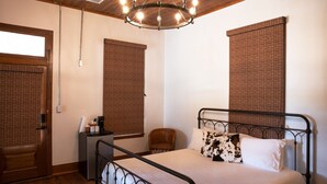 A bedroom with a metal bed frame, a wooden door, a small bedside table with a lamp, and a ceiling light fixture.