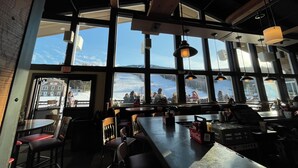 Un restaurante con amplios ventanales, vigas de madera y mesas con sillas.