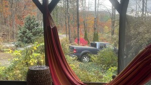 Una hamaca en una habitación con vistas a un bosque y un vehículo afuera.