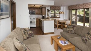 A cozy living room with a sofa, a coffee table, and a dining area with a kitchen in the background. - Village Inn Plaza 103 (Vail)