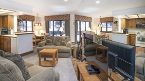 A spacious living area with a fireplace, a television, and a kitchen area with wooden cabinets and a microwave. - Village Inn Plaza 103 (Vail)