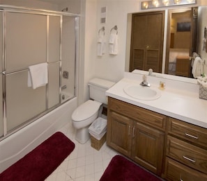 A bathroom with a glass-enclosed shower, a toilet, a sink with a mirror above it, and wooden cabinets. - Village Inn Plaza 103 (Vail)