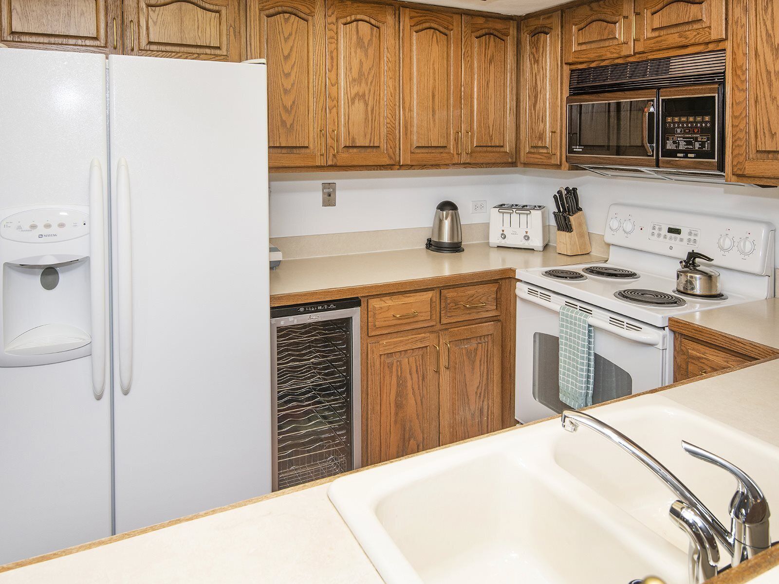 A kitchen with wooden cabinets, a white refrigerator, a microwave, a stove, a dishwasher, and a sink.