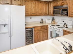 A kitchen with wooden cabinets, a white refrigerator, a microwave, a stove, a dishwasher, and a sink. - Village Inn Plaza 103 (Vail)