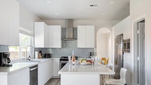 Una cocina moderna con armarios blancos, una isla central, electrodomésticos de acero inoxidable y un comedor con sillas.