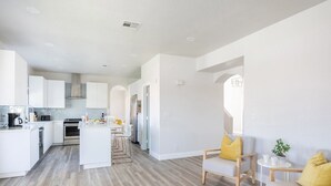 Una cocina moderna con armarios blancos, una isla central y una zona de comedor con sillas amarillas.