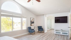 Un dormitorio amplio con una cama grande, dos sillones, un televisor y un vestidor.