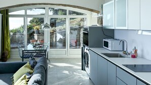 Una cocina moderna con horno integrado, microondas y lavamanos. Hay una zona de comedor con una mesa y sillas, y un ventanal que ofrece vistas al exterior.