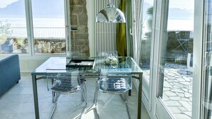 Un comedor moderno con una mesa y sillas de vidrio, una lámpara colgante y vistas a montañas a través de grandes ventanales.